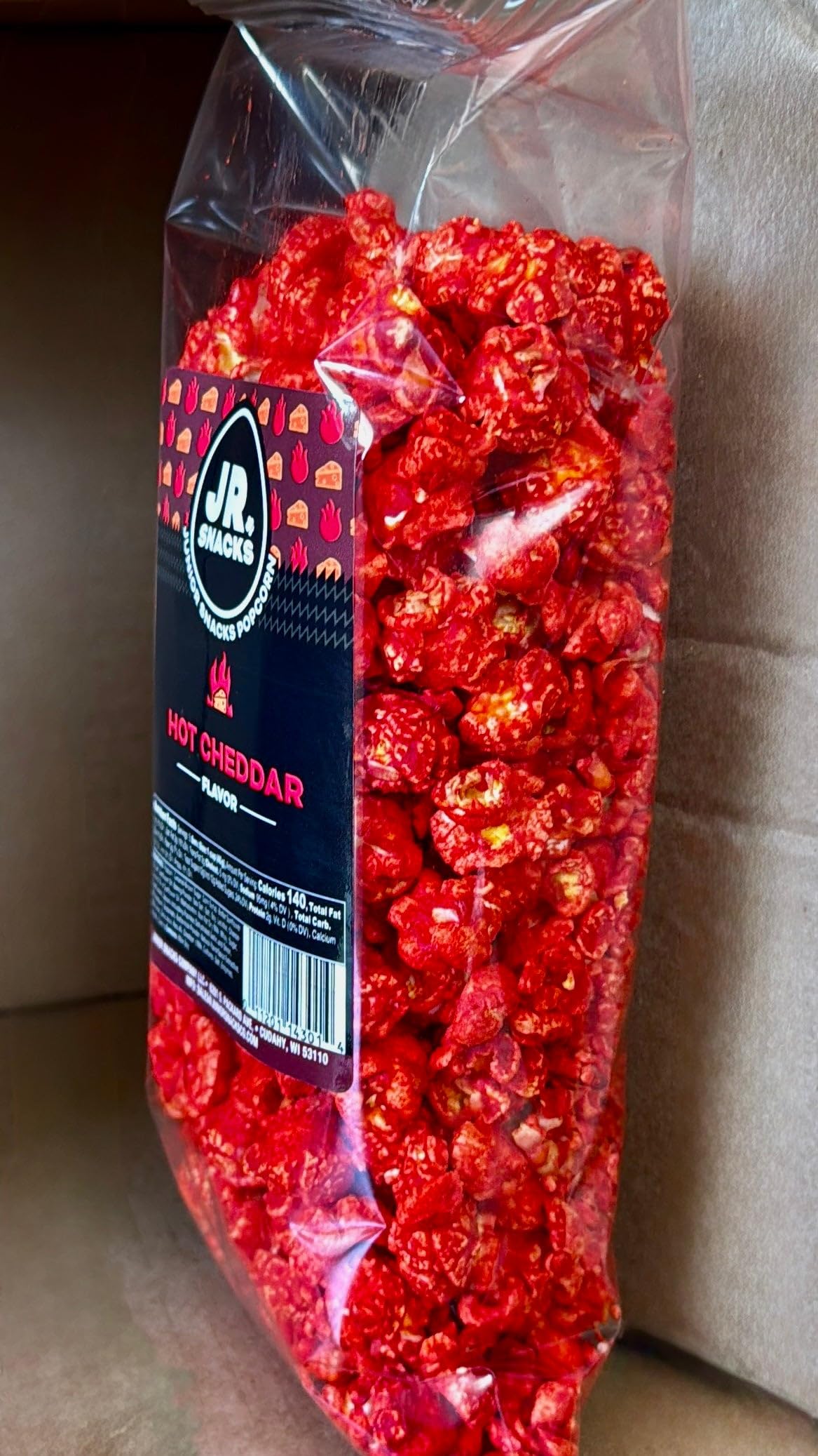 Hot Junior Snacks Co. Hot Cheddar – Spicy snack in a transparent bag showcasing bright red popcorn.