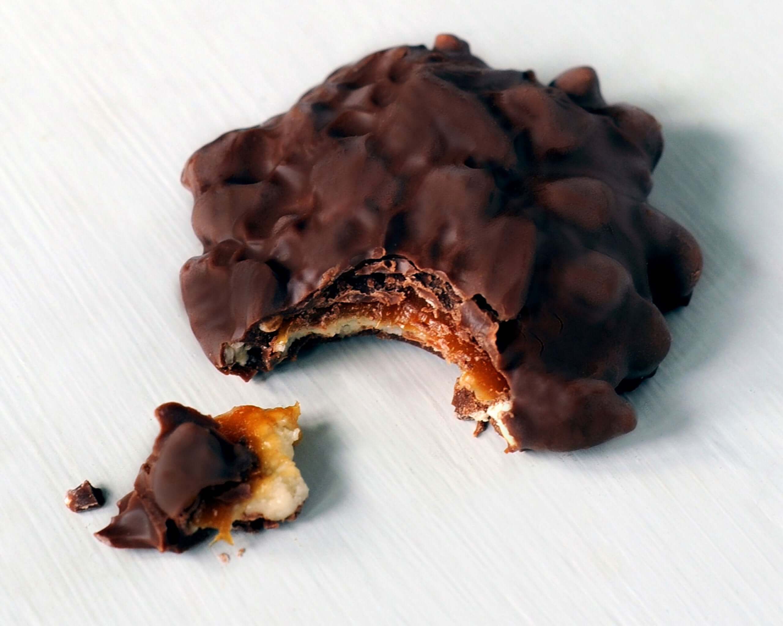 GooGoo Clusters candy bar with a bite taken out, showcasing chocolate coating and caramel filling.